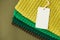 Stack of knitted material from threads of yellow, green, brown colors with blank Price Tag on a blue background. Top view. Copy,