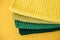 Stack of knitted material from threads of yellow, green, brown colors on a yellow background. Copy, empty space for text