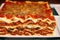 A stack of lasagna with a slice of lasagna on top on a wooden table. Generative AI