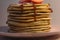 A stack of lush homemade pancakes sprinkled with jam and decorated on top with halves of strawberries and icing sugar. Mouth-