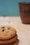 Stack oatmeal cookies with chocolate crisps and brown ceramic glass of milk on wooden table