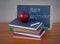 Stack of old books with an apple, a blackboard, chalk and a ruler in front of wooden background. Back to school message.