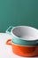 Stack of orange and turquoise ceramic cocottes on white wood table green wall background. Cooking baking cookware concept