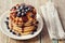 Stack of pancakes or fritters with chocolate sauce and frozen blueberries in a white plate on a wooden rustic table