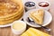 Stack of pancakes in plate, bowl with condensed milk, bowls with jams, napkin, pancake, teaspoon in saucer on table