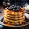 A stack pancakes topped with fresh blueberries and drizzled with syrup on background