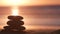 Stack of pebble stones, sandy ocean beach, sunset sky. Rock balancing by water.