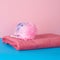 Stack of pink folded towels and a plastic washcloth on a blue background