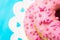 Stack of pink glazed doughnuts with sugar sprinkles on white cake stand with hearts, light blue background, copyspace, birthday, c