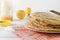 Stack of round Russian pancakes on a plate, a kitchen spatula on an orange towel on a white , jar of honey, lemons, side view