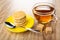 Stack of round wafers with filling, spoon in saucer, sugar, cup of tea on wooden table