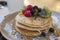 Stack of thick, fluffy American-style pancakes served with maple syrup poured over fresh berries and kiwi