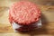 Stack of three fresh uncooked beef burgers separated with cooking paper on a cutting wooden board and table. Food industry