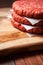 Stack of three fresh uncooked beef burgers separated with cooking paper on a cutting wooden board and table. Food industry