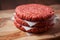 Stack of three fresh uncooked beef burgers separated with cooking paper on a cutting wooden board and table. Food industry