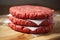 Stack of three fresh uncooked beef burgers separated with cooking paper on a cutting wooden board and table. Food industry