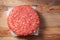 Stack of three fresh uncooked beef burgers separated with cooking paper on a cutting wooden board and table. Food industry. Top