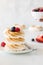 A stack of toasted meringues and berries with a hand holding a small bowl of berries in behind.