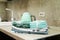 Stack of various kitchen towels and a turquoise electric kettle in a bright kitchen with a sink