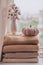 A stack of warm knitted sweaters on the windowsill with pumpkin and a vase of cotton plant in pastel shades