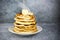 Stack of warm pancakes with steam on white plate with piece of butter, sliced banana and maple syrup on gray surface