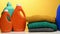 Stack of washed folded clothes and plastic orange large bottles with liquid detergent stand on a white table, yellow background. R