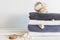 A stack of white bath towels with blue tape and different seashells near jar with seashells on white wooden table. Spa