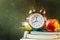 Stack of workbooks pens pencils alarm clock red apple on vintage scratched chalkboard background. Back to school education