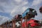 Stacked cars on a metallic frame, used for parts. Scrapyard perspective with blue skies and fluffy clouds.