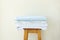 Stacked clean folded cotton bedlinen on wooden stool white wall background. Laundry washing cleanliness concept