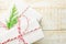 Stacked gift boxes wrapped in white paper tied with striped red ribbon green juniper twig on plank wood background. Christmas