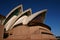 Stacked white shells of curved and pointy roofs with exposed concrete beams on pink podium of Sydney Opera House Australia