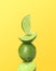 Stacked whole and cut limes on yellow background