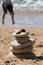 Stacked zen stones on sandy beach with quiet sea waters and small boy running back to waterfront