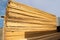 Stacks of edged softwood boards of yellow color against a blue sky background. Construction