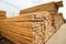 Stacks of timber and edged boards of coniferous wood are yellow against the blue sky. Construction production