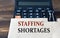 STAFFING SHORTACES - words on light brown paper on calculator background