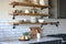 Stage shelves in a kitchen featuring minimalist black metal pipe brackets that are one rod and feature a circular base on the wall