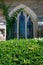 A Stained Glass Window On a Cobblestone Church With Ivy Climbing Up Its Side