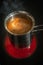Stainless steel cezve with coffee in process of making standing at hot and red electrical stove in darkness, closeup, details