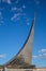 A stainless steel obelisk for space explorers in the form of a rocket taking off against a blue sky background.