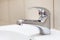 Stainless water tap in bathroom sink, white sanitary and wall with beige tiles