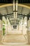 Staircase along exterior hallway corridor with high ceiling, lights and fixtures above and along stone wall columns