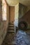 Staircase, with old truck tyre underneath, in an old derelict cottage. Floor strewn with peeled paint and wallpaper, with old with