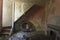 Staircase, with old truck tyre underneath, in an old derelict cottage. Floor strewn with peeled paint and wallpaper, with old fire