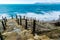 A staircase with stone steps and rope handrails leads down to the green stormy sea. On the horizon mountains and ships