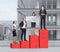 Stairs as a huge red bar chart are on the roof. Business people are standing on each step as a concept of corporate ladder. A pano
