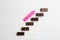 Stairs made of blocks and pink arrow on wooden background, flat lay. Career promotion concept