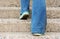 stairway. Close up legs flared jeans and shoes sneakers  of young woman One person walking stepping going up the stairs
