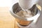 Stand mixer in action is stirring dough with the dough hook in a stainless steel bowl on a wooden kitchen workspace, motion blur,